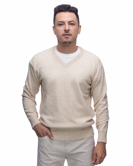 A man wearing a cream v-neck knit sweater over a white undershirt and off-white trouser, standing against a plain white background.