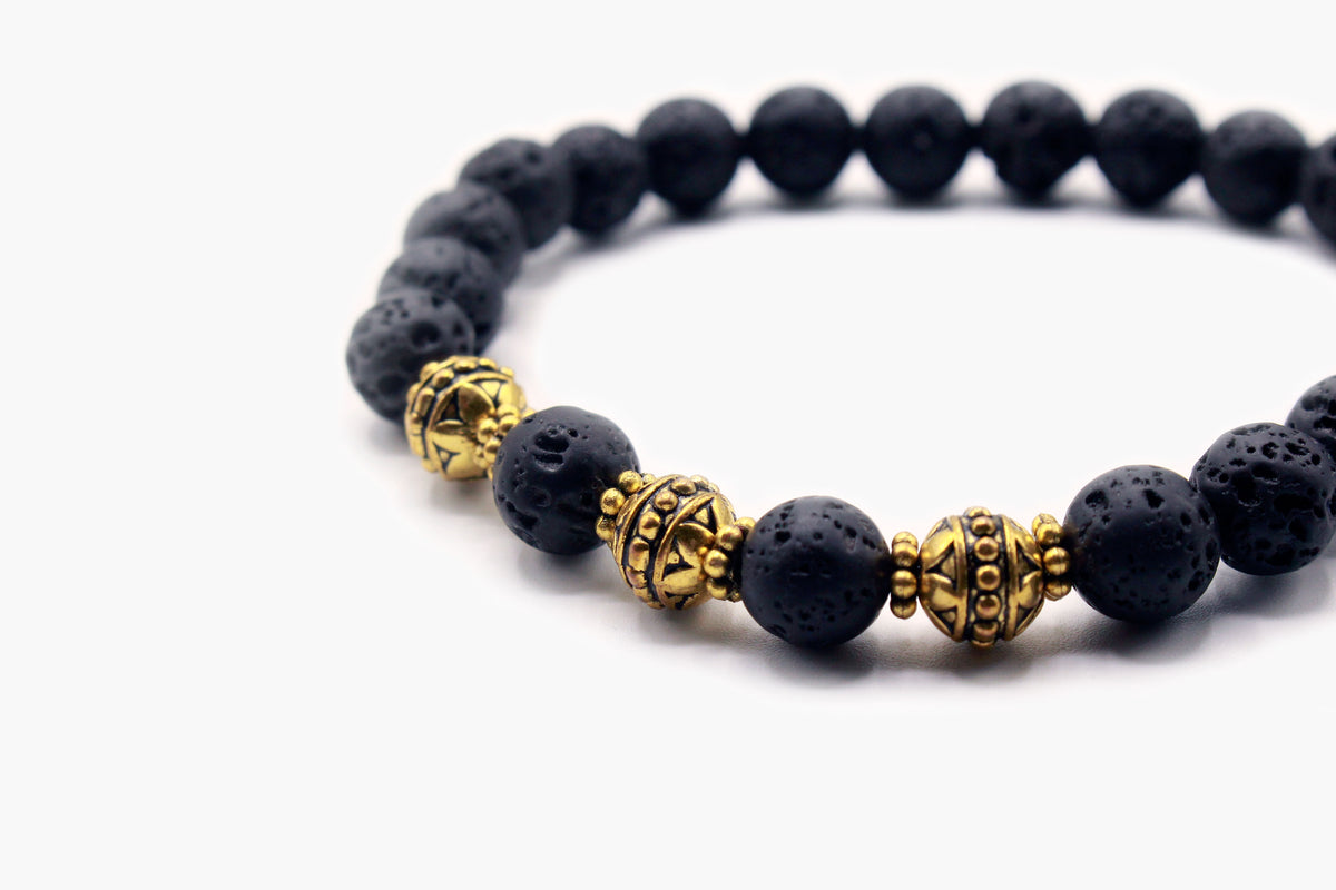 Close-up of porous black Lava Stone beads with gold-tone decorative accents.
