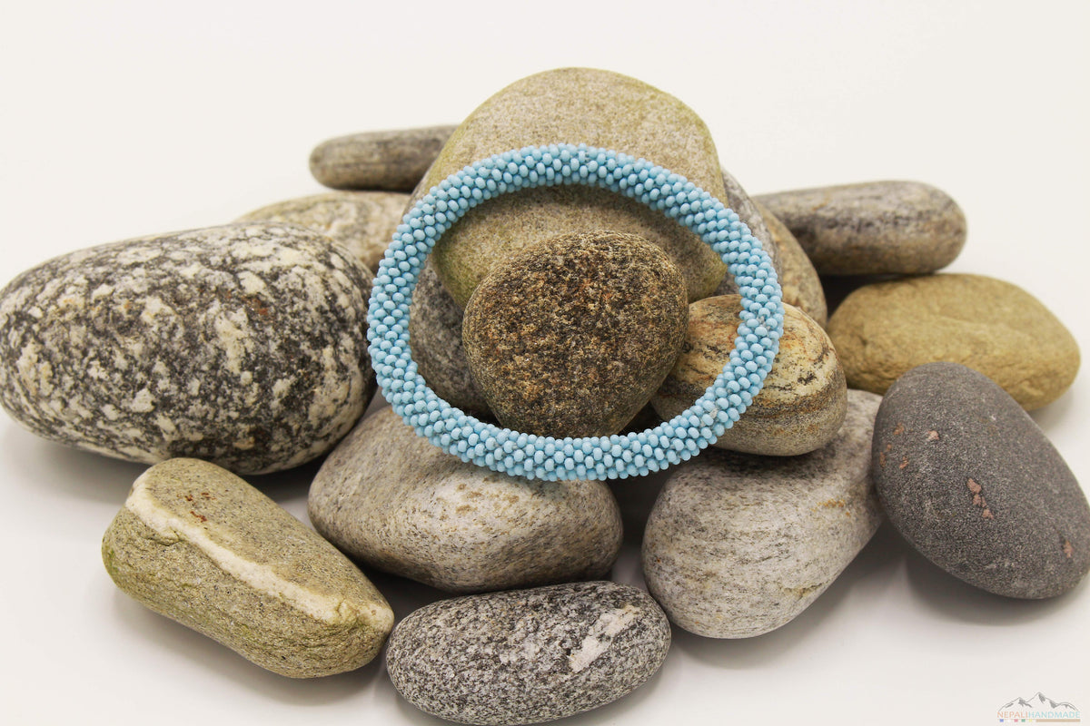 Light blue glass bead roll-on bracelet displayed on natural stones.