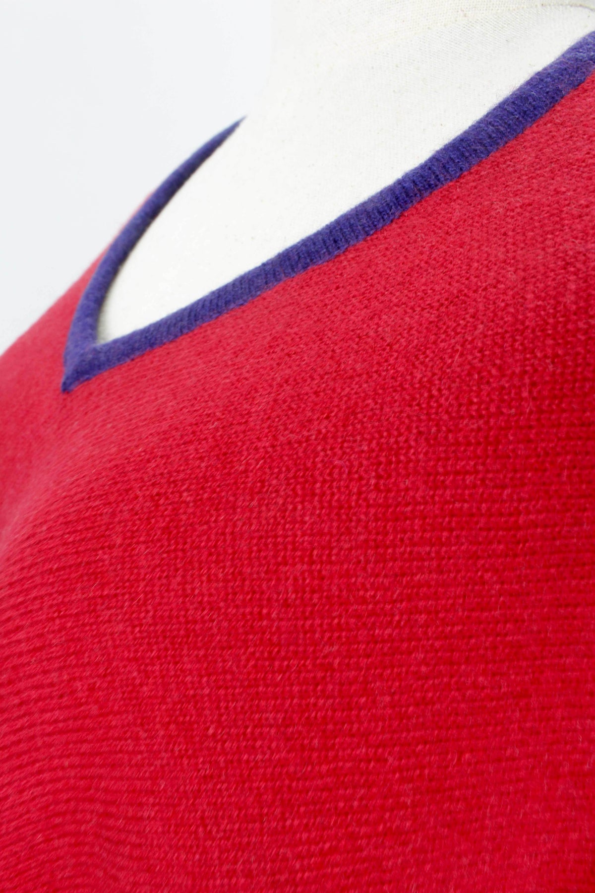 Close-up of the women's red cashmere poncho showing the royal blue V-neck trim and fabric texture.