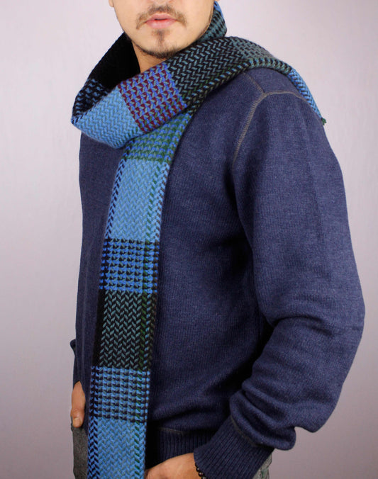 Man wearing a 100% cashmere wool herringbone scarf in shades of blue, posed sideways with the scarf loosely draped in a half-loop