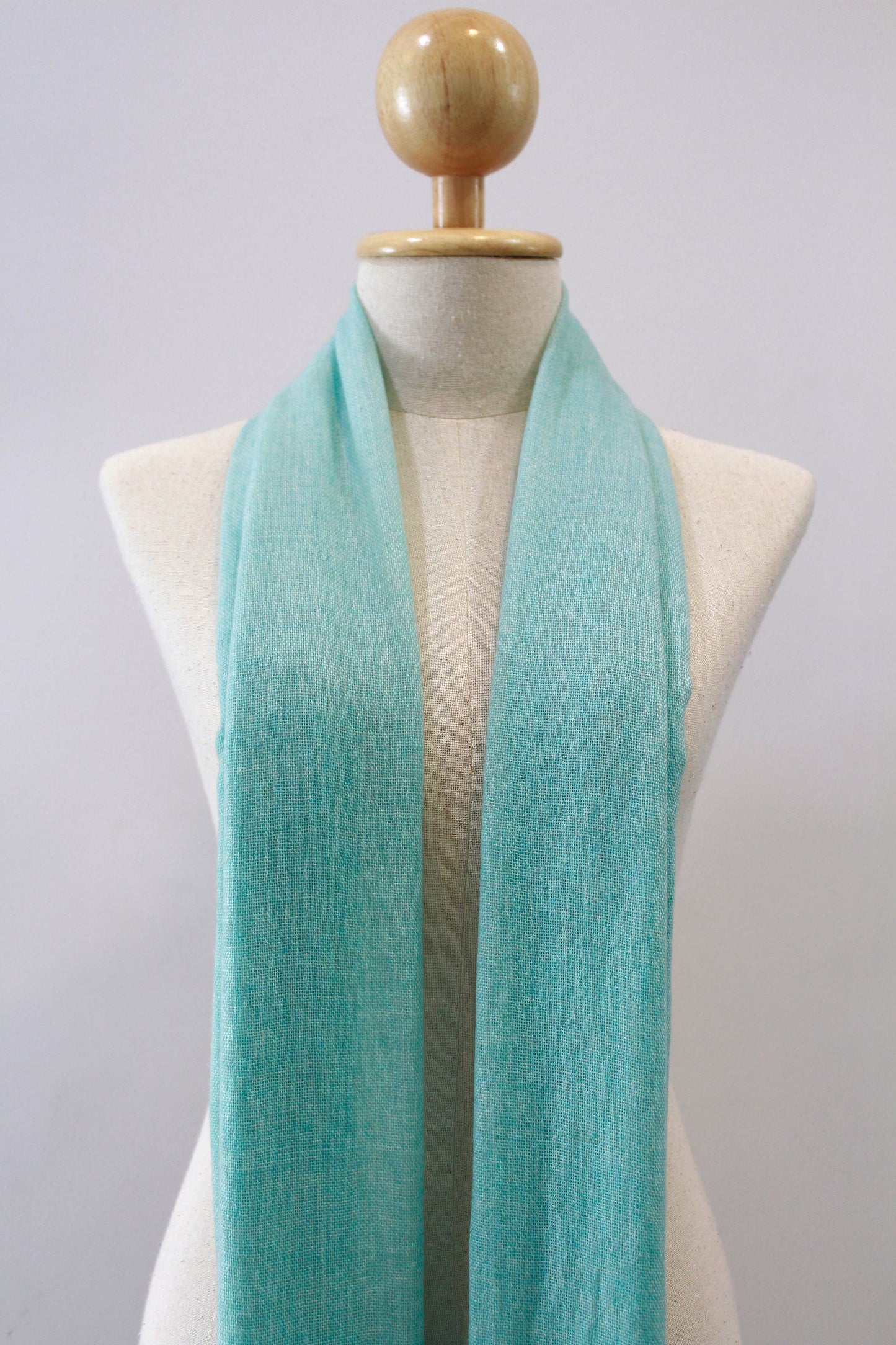 Mint green cashmere scarf draped loosely around the neck of a mannequin, front view.