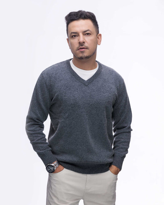 A man wearing a charcoal gray v-neck knit sweater over a white t-shirt and beige trousers, standing against a plain white background.
