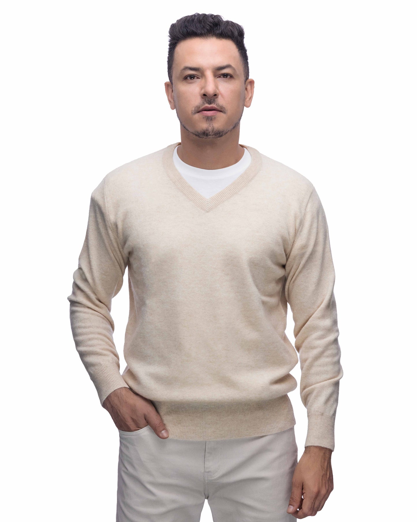 A man wearing a cream v-neck knit sweater over a white undershirt and off-white trouser, standing against a plain white background.