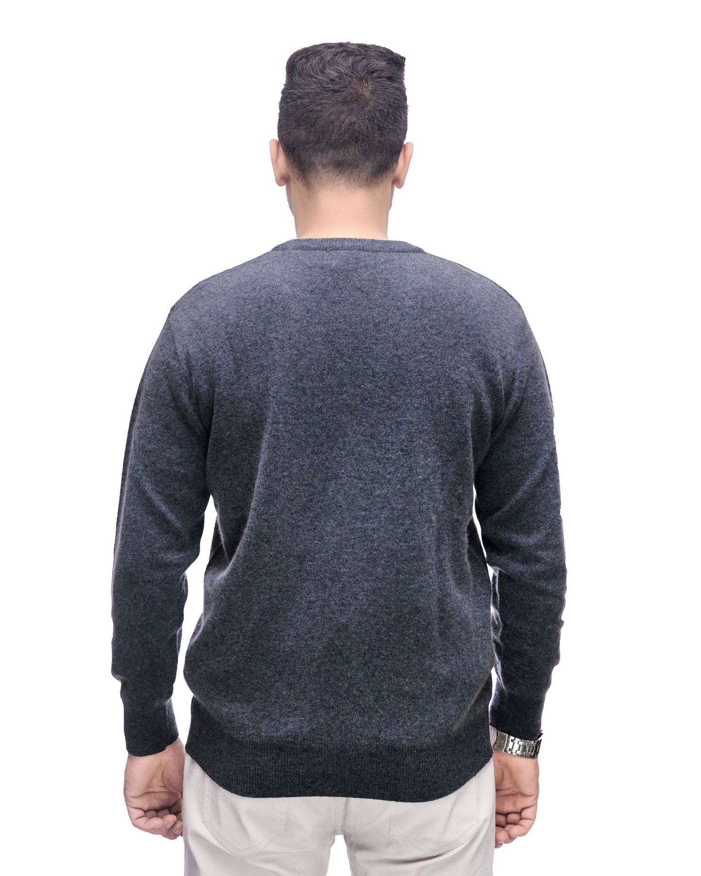 A man viewed from behind wearing a dark gray heathered knit sweater and off-white trousers, standing against a plain white background.
