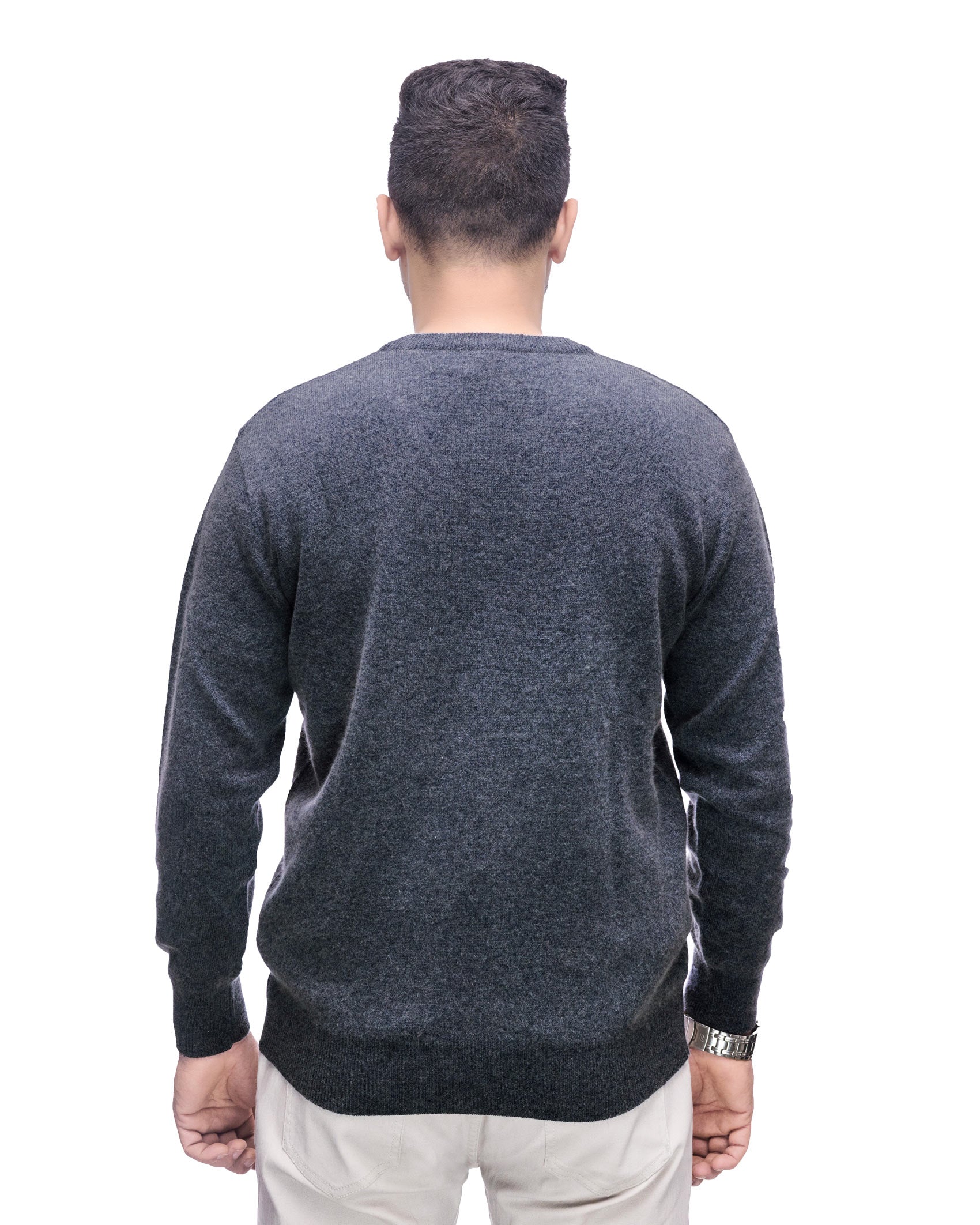 A man viewed from behind wearing a dark gray heathered knit sweater and off-white trousers, standing against a plain white background.