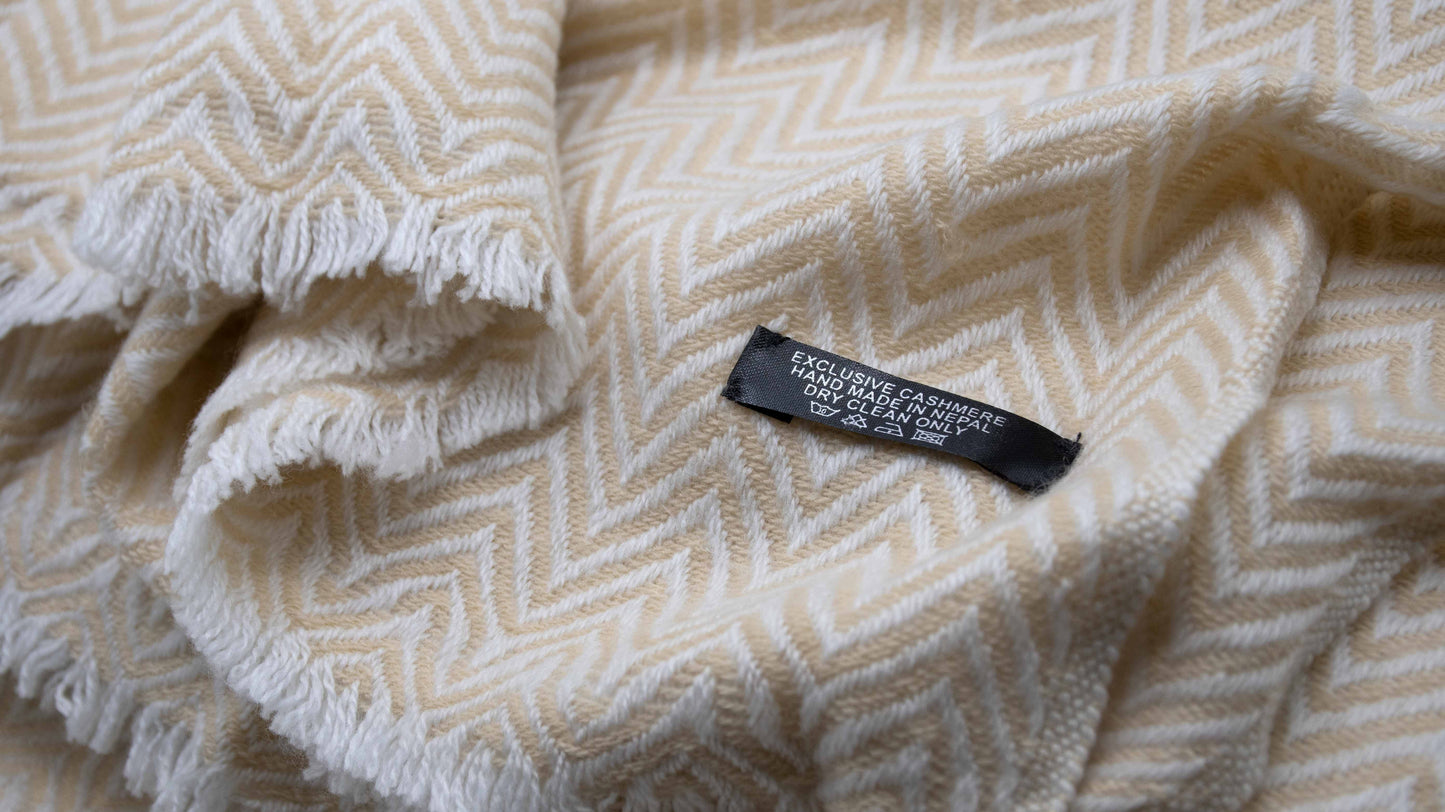 close up picture of Yellow And White Chevron Cashmere Blanket zoomed showcasing the weaving details and tag which mentions exclusive cashmere that is handmade in nepal and also suggests to dry clea only