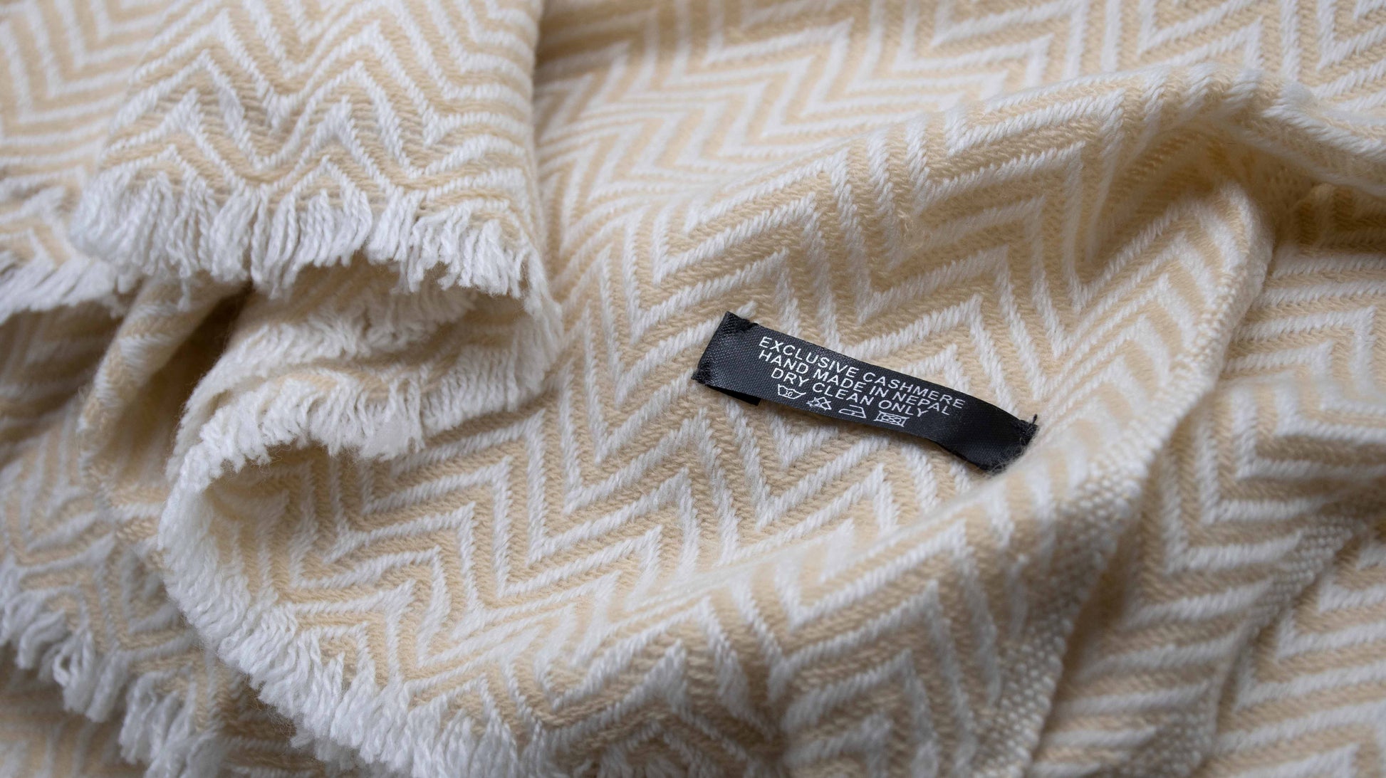 close up picture of Yellow And White Chevron Cashmere Blanket zoomed showcasing the weaving details and tag which mentions exclusive cashmere that is handmade in nepal and also suggests to dry clea only