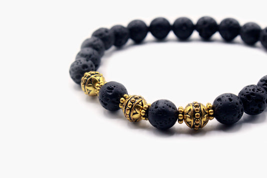 Close-up of porous black Lava Stone beads with gold-tone decorative accents.