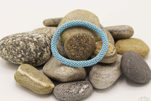 Light blue glass bead roll-on bracelet displayed on natural stones.