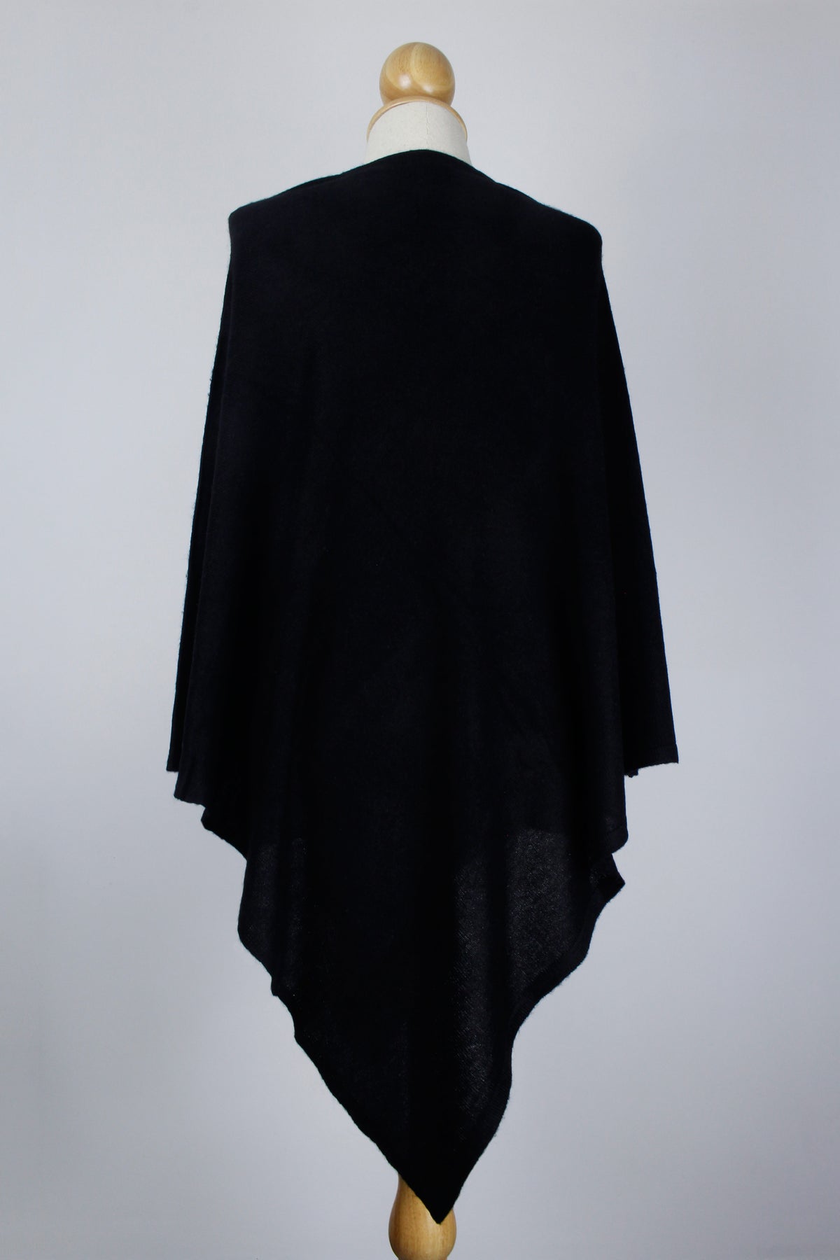 Women's black cashmere poncho displayed on a mannequin, back view showing the draped silhouette.