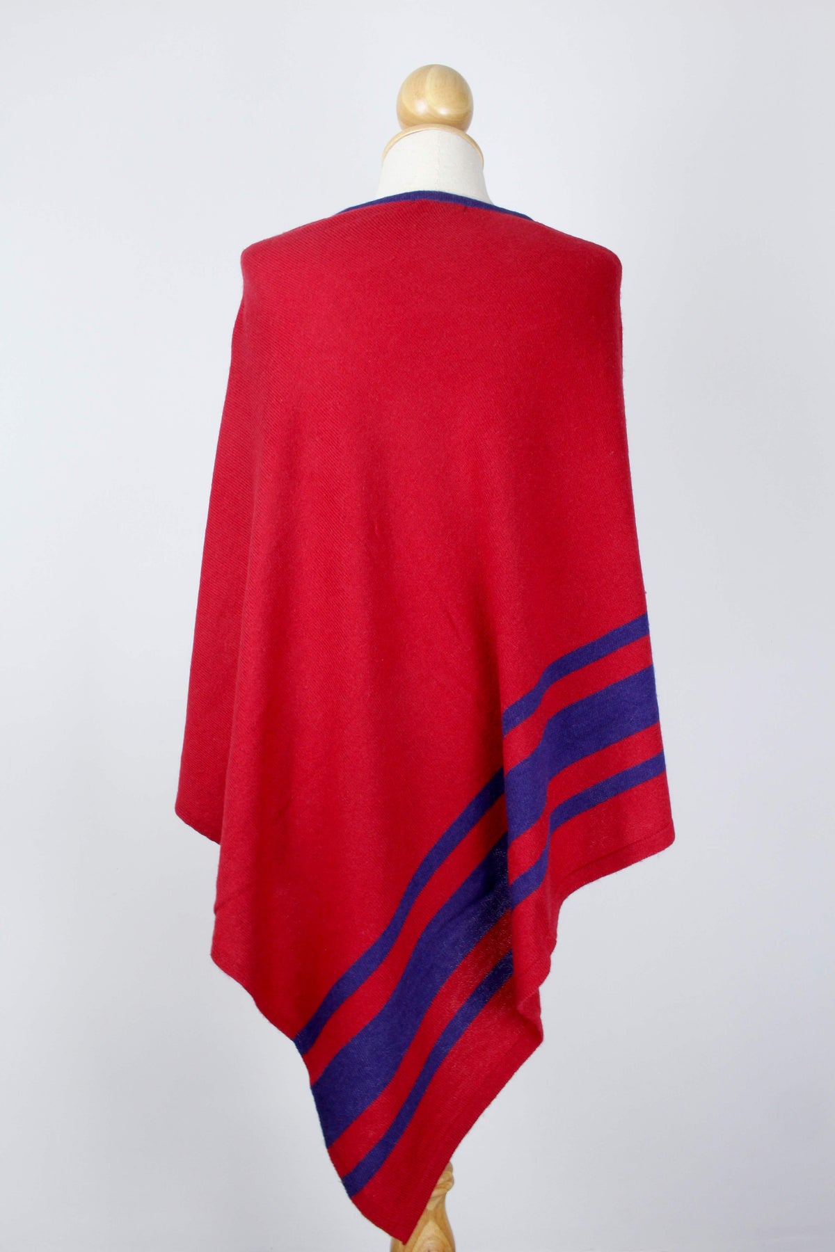 Women's red cashmere poncho displayed from the back with royal blue stripe detailing along the lower section.