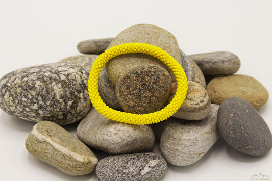 Bright yellow glass bead roll-on bracelet displayed on natural stones.