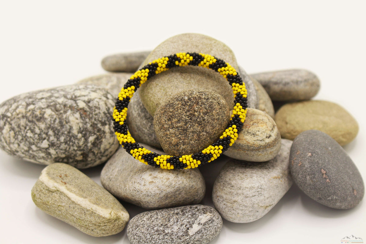 Black and yellow patterned glass bead roll-on bracelet displayed on natural stones.