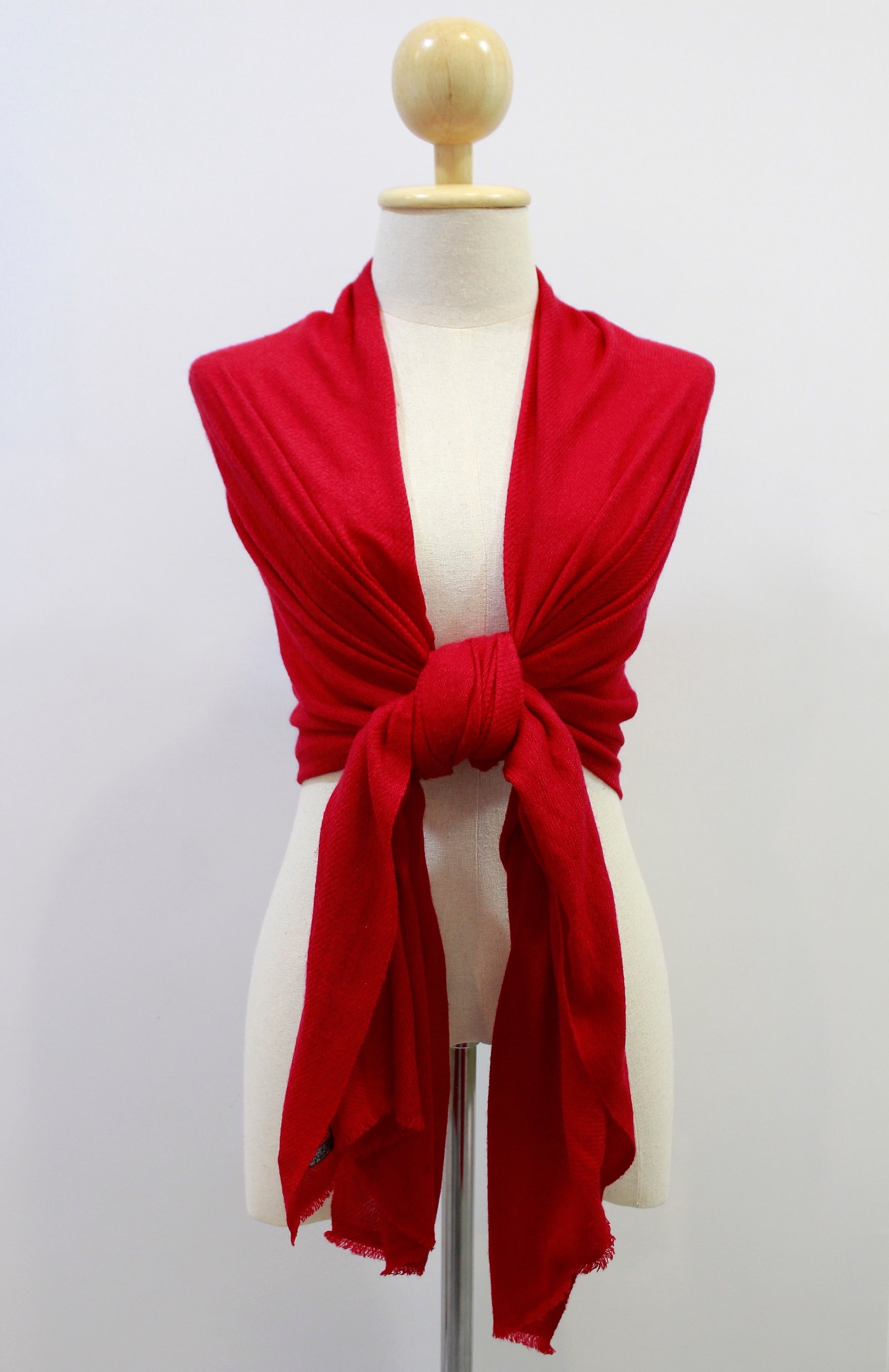 Crimson red cashmere scarf draped over the shoulders and styled with a front knot on a display mannequin against a white background