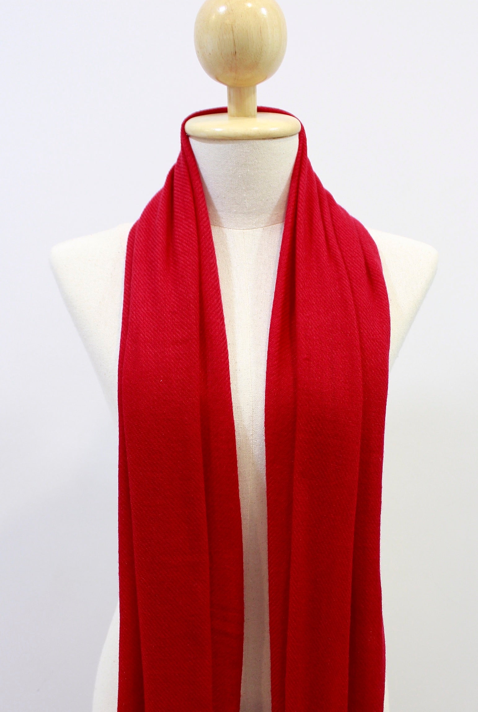 Crimson red hand-loomed cashmere scarf shown in an open shoulder drape on a display mannequin against a white background, showing its weave texture and length