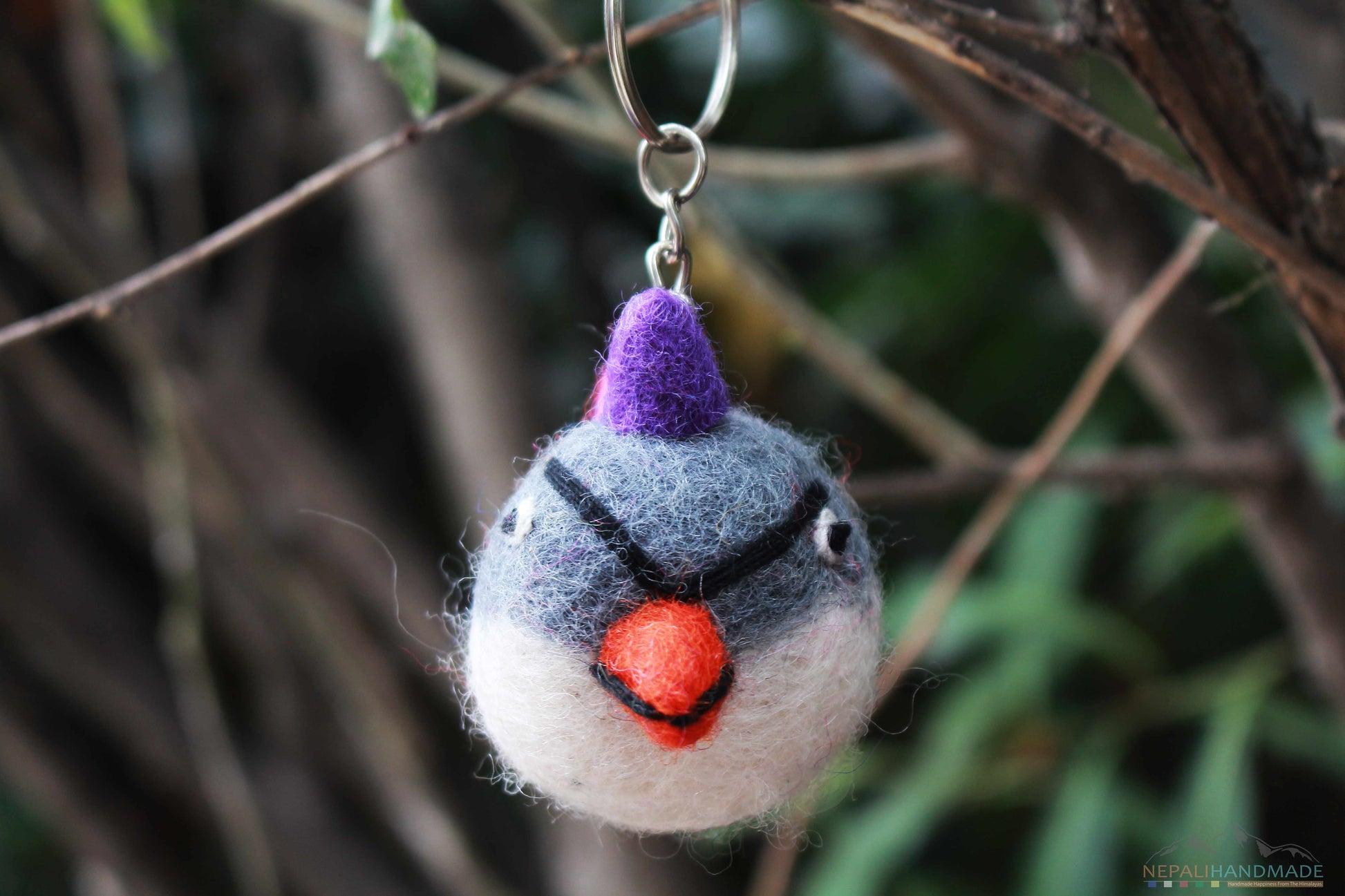 gray and white colored angry bird keychain handmade from felted merino wool, hung at a tree branch