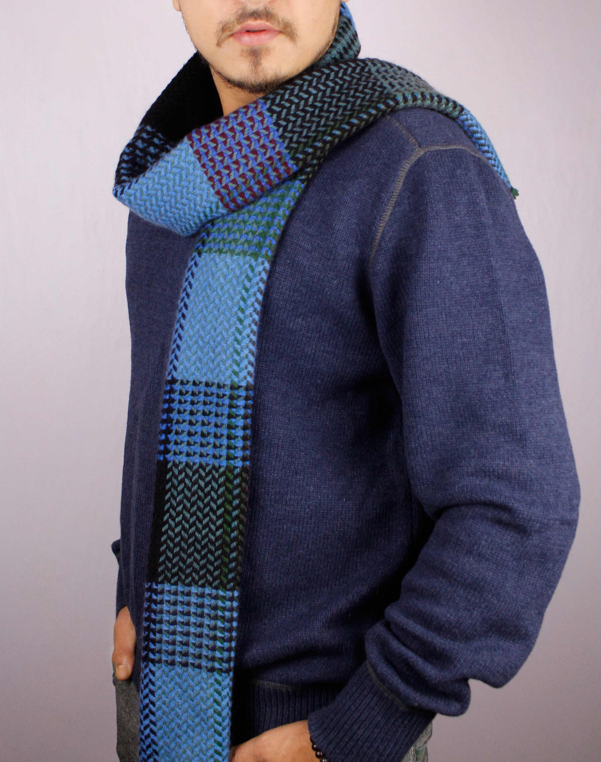 Man wearing a 100% cashmere wool herringbone scarf in shades of blue, posed sideways with the scarf loosely draped in a half-loop 