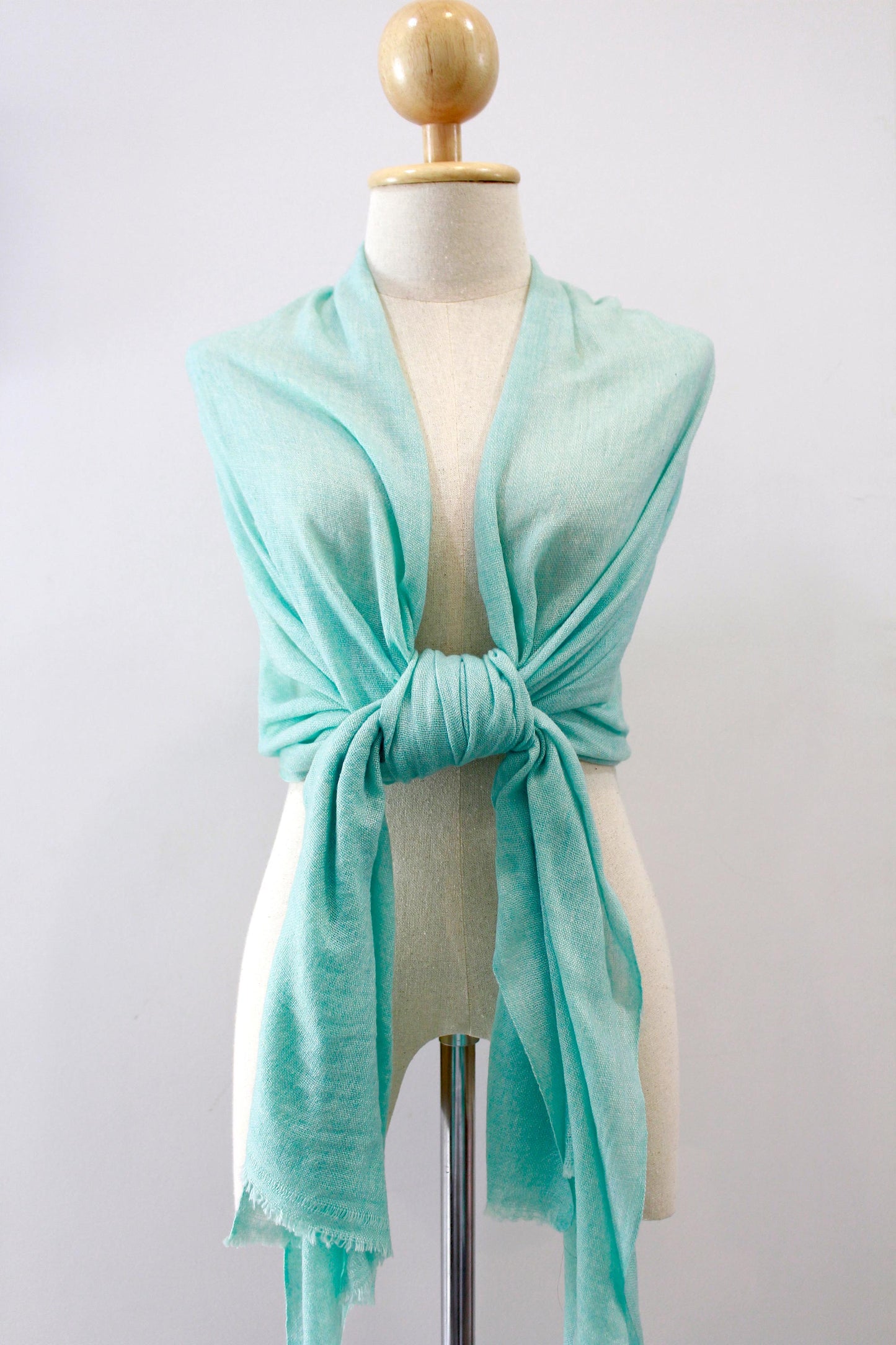Mint green cashmere scarf draped over the shoulders and tied at the front on a mannequin.